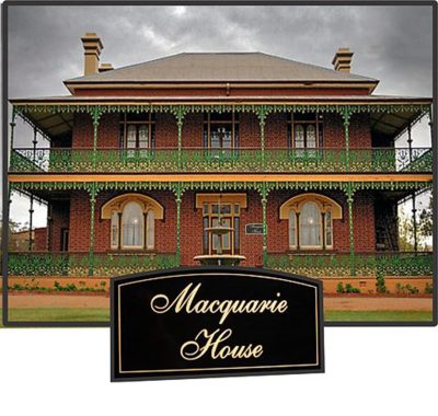Historic two-story brick heritage home with intricate green wrought iron balconies and a custom black arched Macquarie House sign in the foreground.
